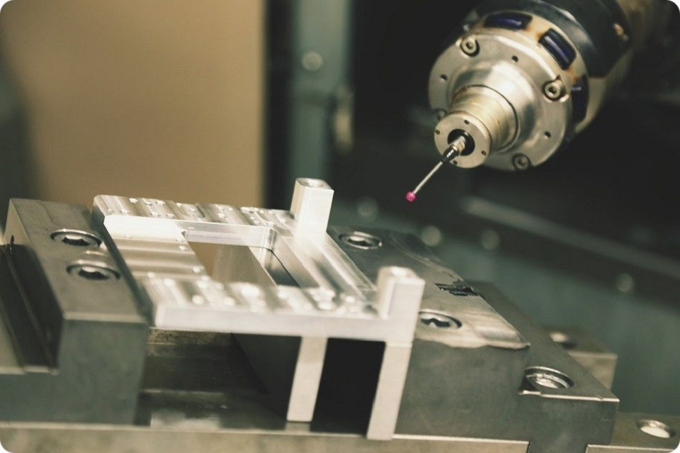 Industrie du futur 4.0 - Modélisation et mesure avec une tête industrielle équipée d'un palpeur avec une bille rouge en extériorité venant prendre une touche sur une pièce usinée en aluminium bridée dans un support. la t